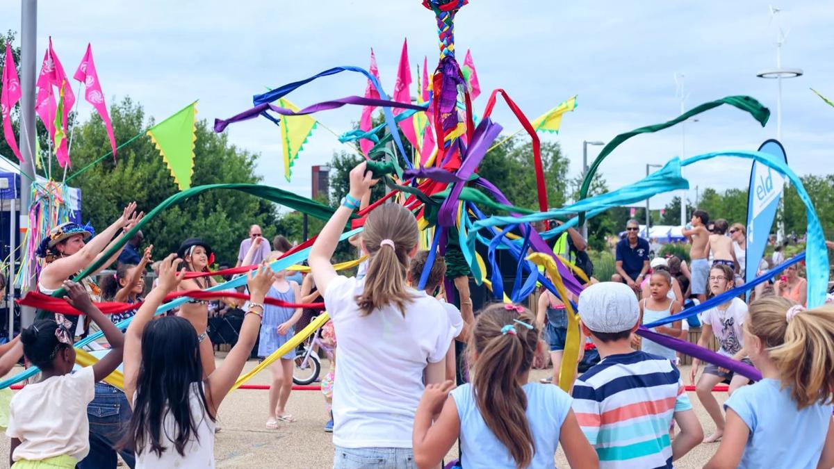 A large group of children and a performer grab multicoloured long materials