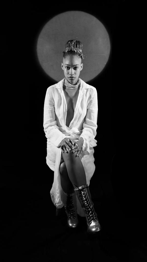 A black woman wearing white sits facing forwards; there is a halo of light around her head