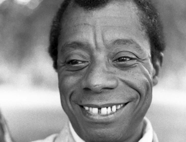Black and white photo of James Baldwin wearing a white shirt and neck scarf