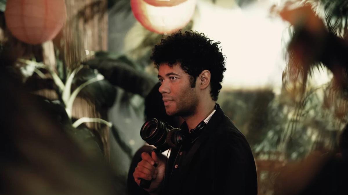 Richard Ayoade holding a camera in a jungle themed room