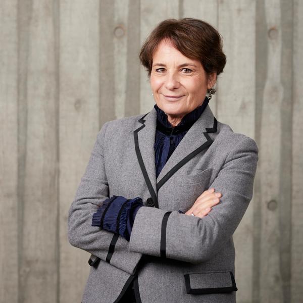 Elaine Bedell, a white woman with short dark hair, stands in front of a concrete wall