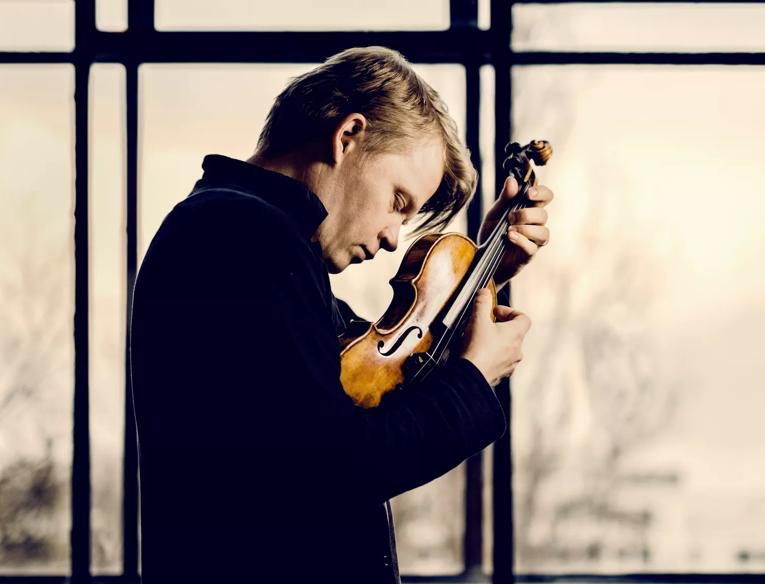 Violinist Pekka Kuusisto holding a violin close to his face