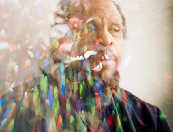 Portrait of musician Fimber Bravo. He is pictured alongside a refracted rainbow of colours. 