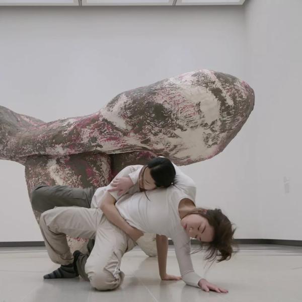 Two dancers, both women with dark hair, move together around the sculptural work 'untitled: girl ii' (2019) by Phyllida Barlow in the Hayward Gallery