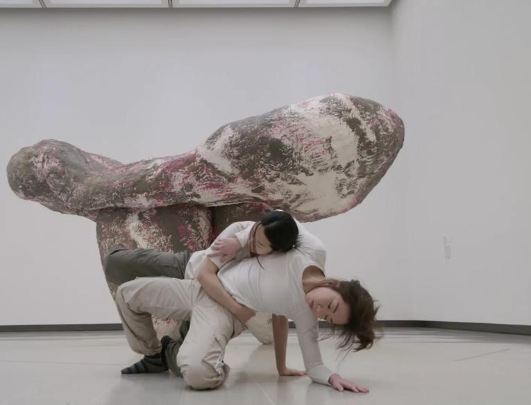 Two dancers, both women with dark hair, move together around the sculptural work 'untitled: girl ii' (2019) by Phyllida Barlow in the Hayward Gallery