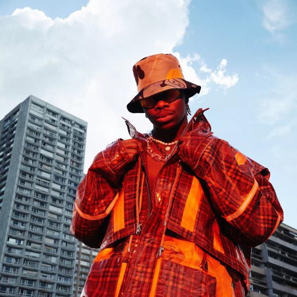A man in an orange and red checked jacket standing in front of a skyscraper.
