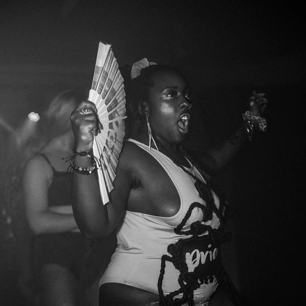 Black and white photo of a Black woman dancing in a leotard and fanning herself. 