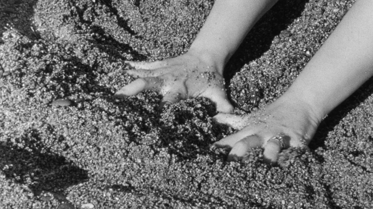Black and white image of a woman's hands in the sand.