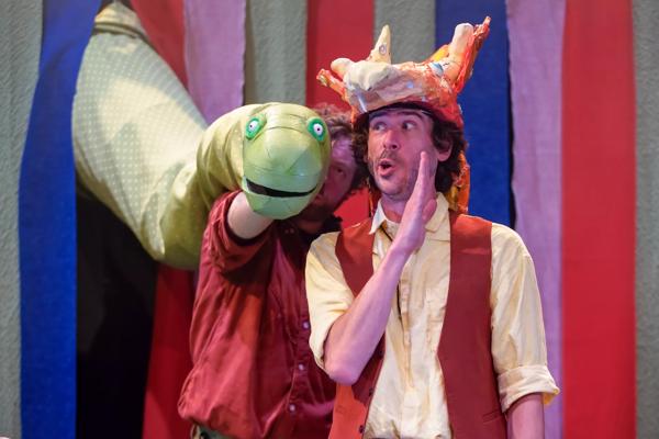 Actor in a dinosaur hat whispers to a green dinosaur puppet.