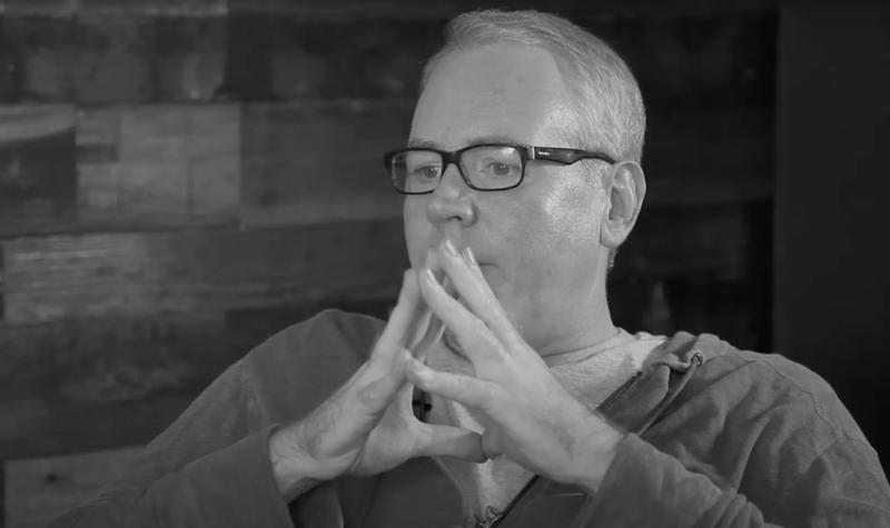 Author Bret Easton Ellis clasps his hands in front of the lower half of his face in a studio