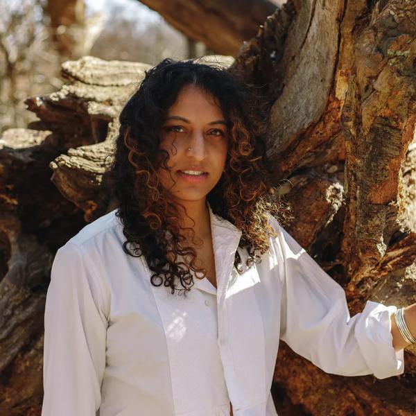 Sheena Patel in a white shirt leaning back on a branch