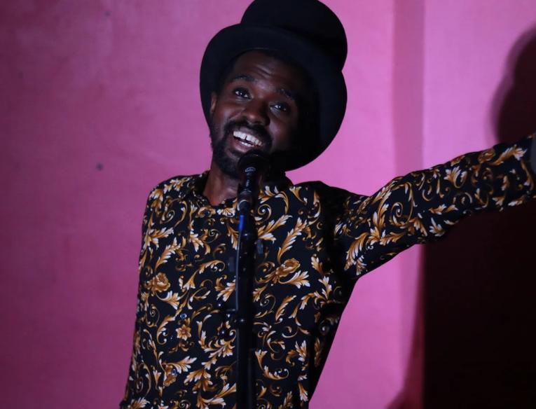 A man wearing a hat and a colourful shirt, performing at a microphone