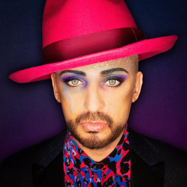 Boy George wearing a pink and blue spotted shirt and a pink hat