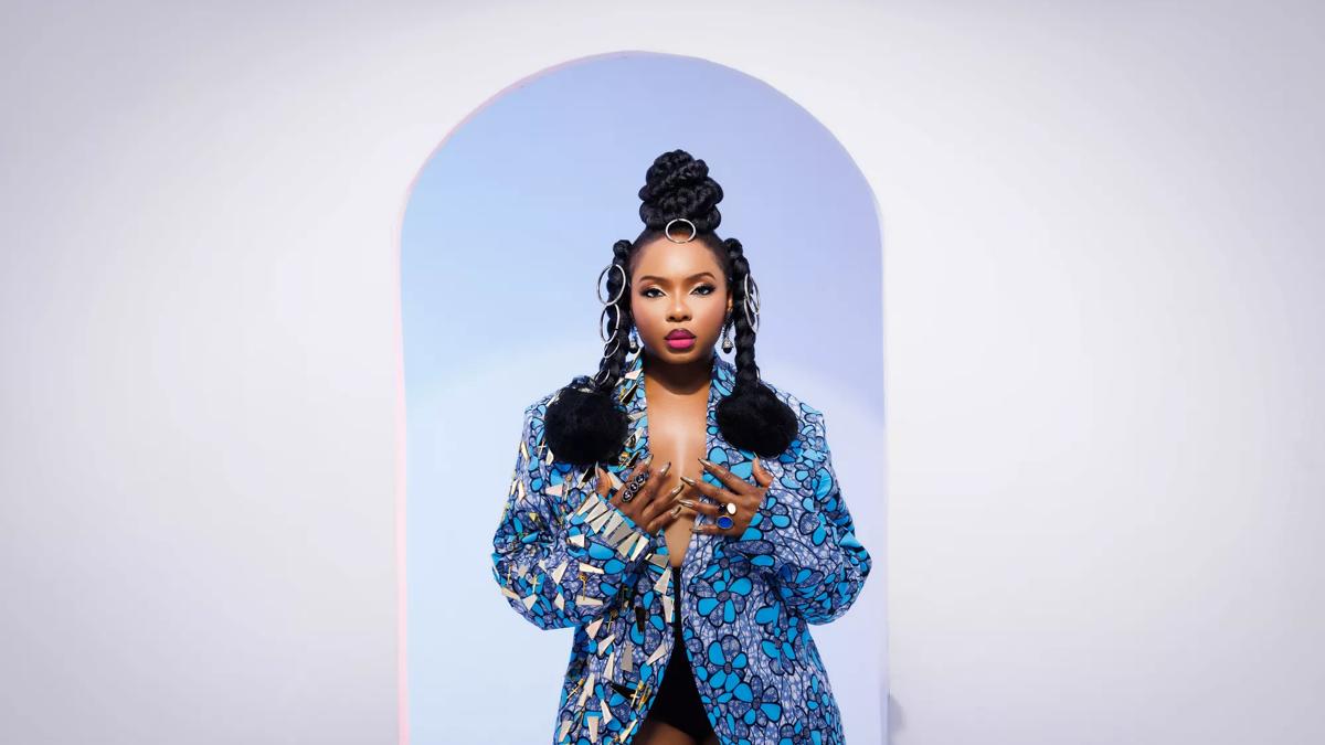 Singer, Yemi Alade pictured wearing a blue printed blazer. Her hair is braided and adorned with silver hooped jewellery. 