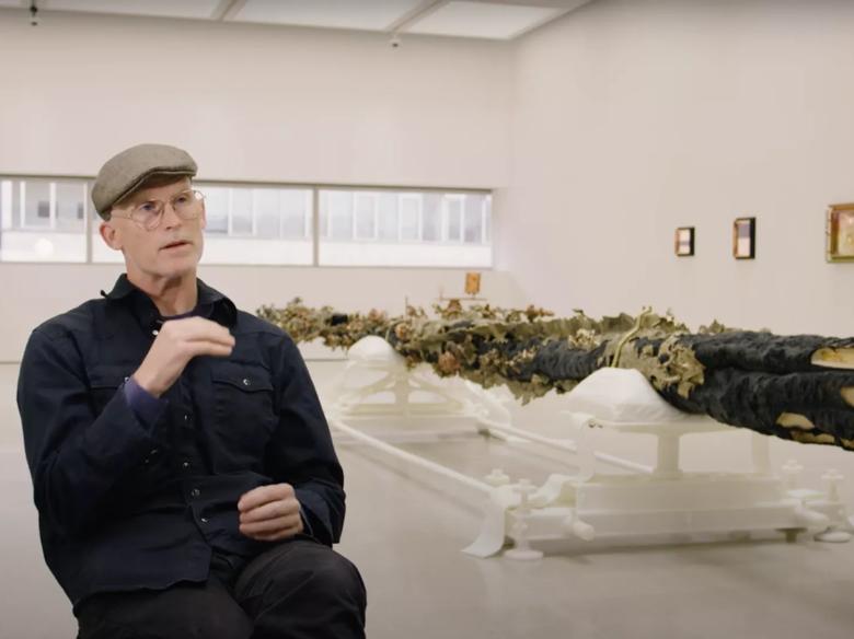Matthew Barney sits talking to camera in his exhibition Redoubt at Hayward Gallery
