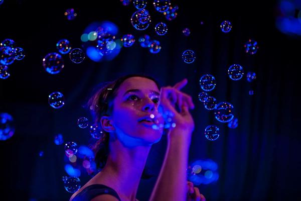 A woman is pointing her finger, ready to burst the bubbles (lit by LED blur light).
