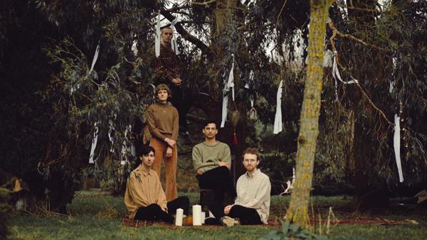Five musicians pose in a clearing in some woods