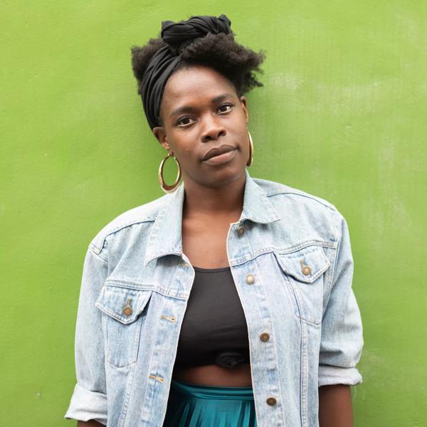 A woman wearing a denim jacket standing against a green background