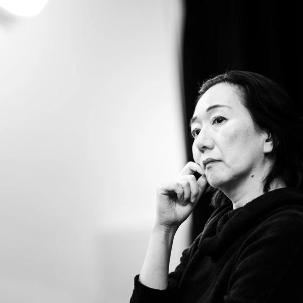 Black and white image of artist Chisato Minamimura looking down with her hand on her face.