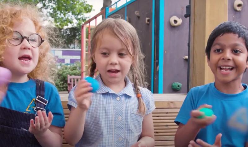 Screengrab from video about Aurora Classroom showing three small children playing with egg shakers