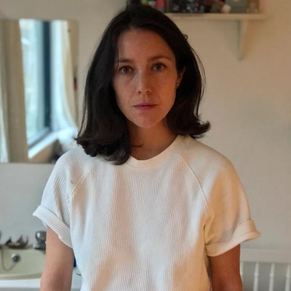 Portrait of writer Daisy Hildyard looking at the camera, wearing a white t-shirt
