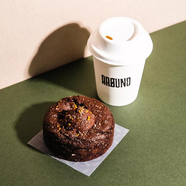 A chocolate and orange cookie and a compostable cup of coffee on a green background