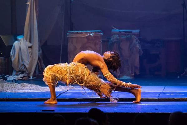 A contortionist in Afrique en Cirque costume in a deep lunge onstage 