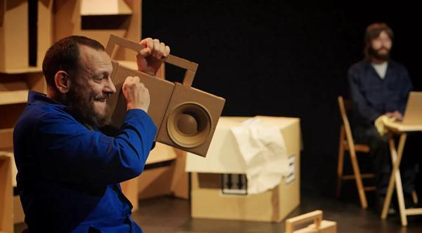 Person wearing blue holding a boombox made out of cardboard to their ear.