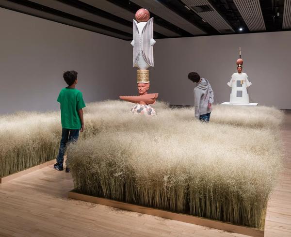 An installation view of a rice field, with sculptures in the middle, and two young children looking at the artwork.