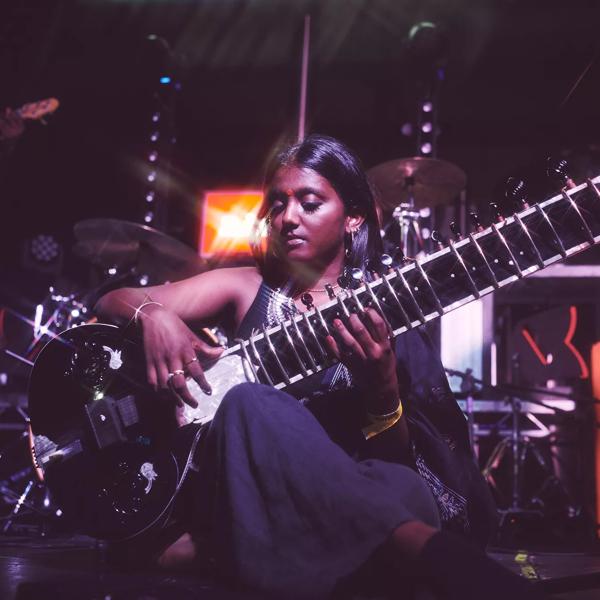 A seated person plays a shiny black sitar