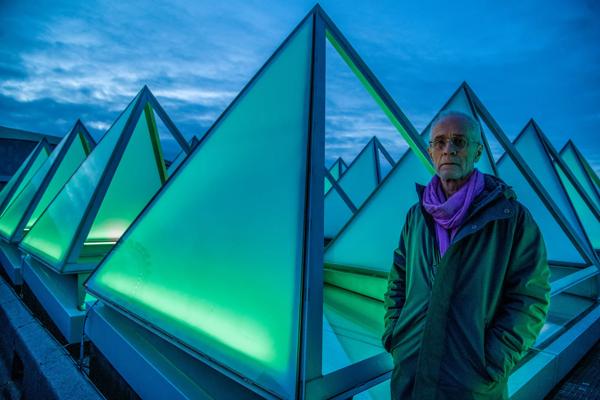 Artist David Batchelor stands on the roof of the Hayward Gallery beside the pyramid windows, illuminated by his installation piece Sixty Minute Spectrum