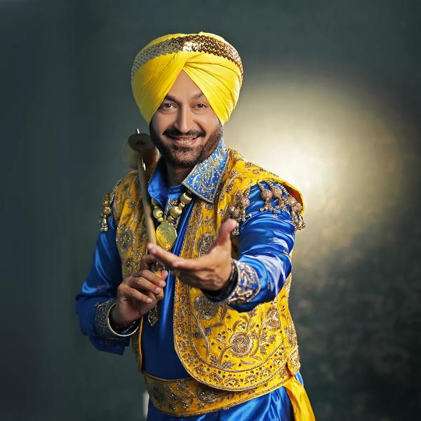 Male presenting person dressed in traditional gold and blue Indian clothing holding their hand out