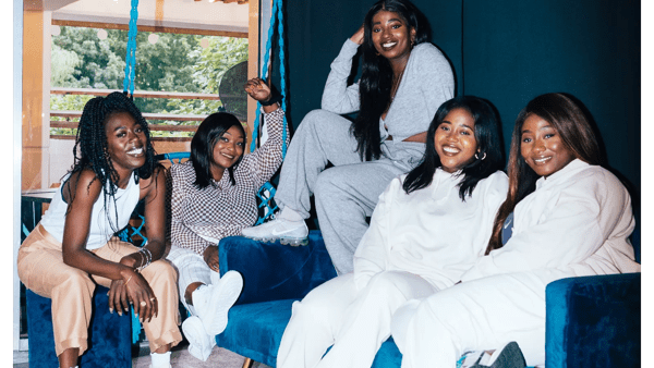 Five radiant, young Black women sitting on blue sofas smile