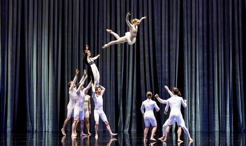 Dancers dressed in white launching another dancer in the air 