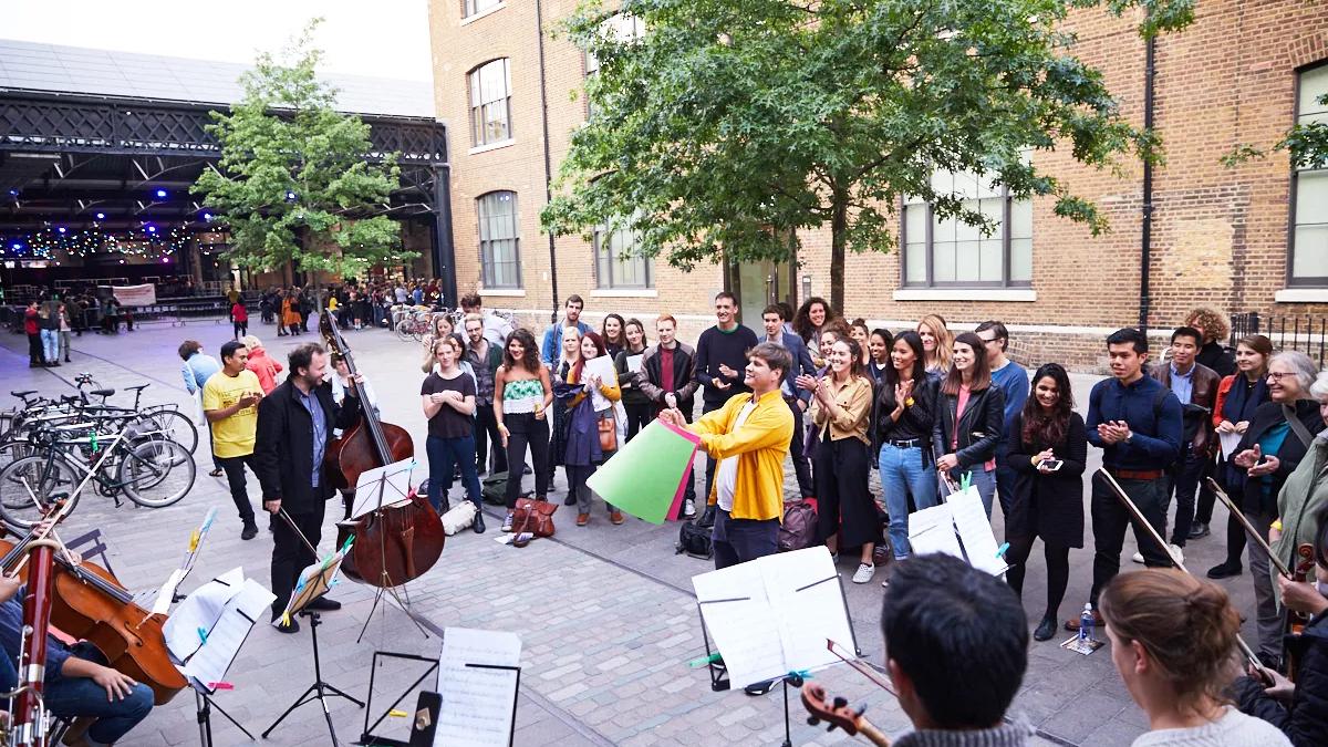 Multistory orchestra performs in open space around Kings Cross area.