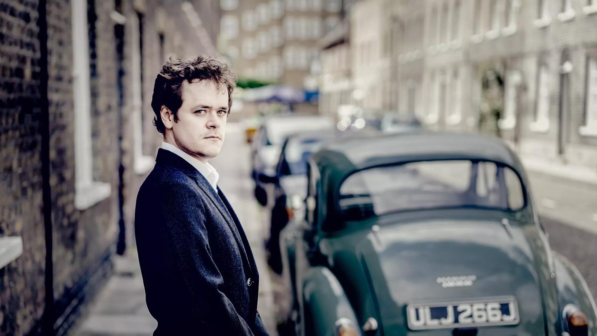 Pianist Benjamin Grosvenor in a suit, photo taken in a neighbourhood street 