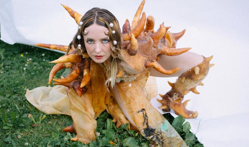 A woman wearing an orange fish suit with spikes with pearls in her hair