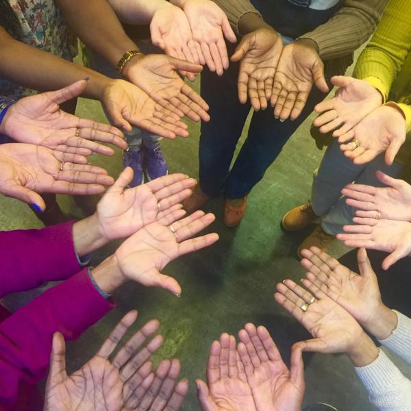 10 people standing in a circle holding their palms up - only their arms and hands are in shot