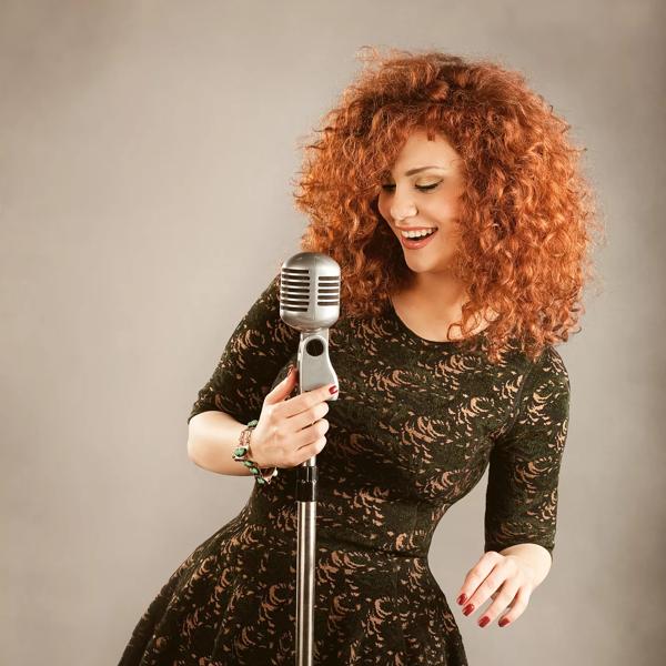 Lena Chamamyan, a woman with red curly hair in a black dress sings into a microphone 