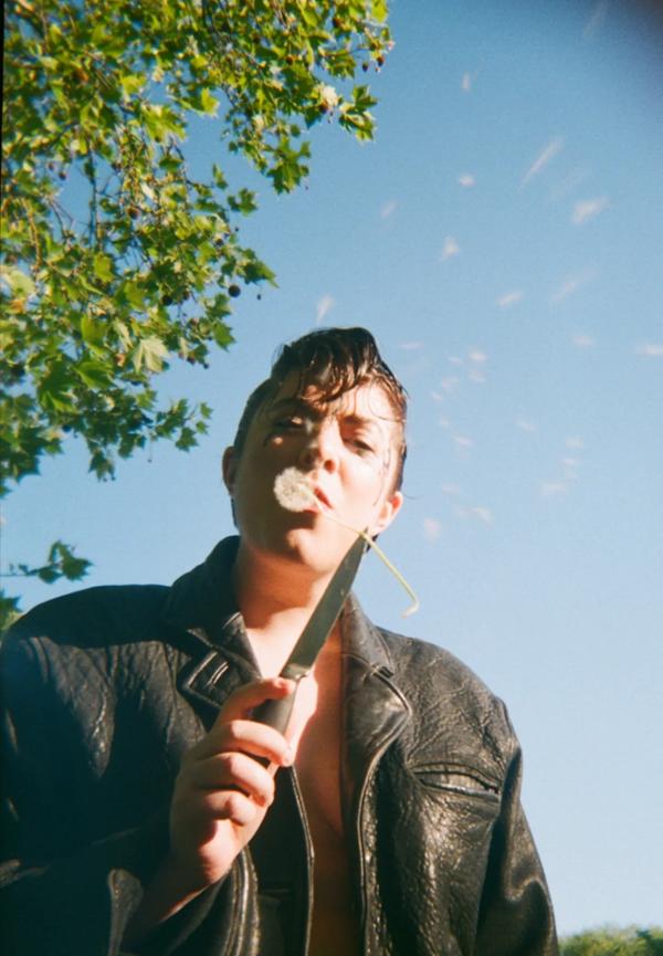 Photo of DJ Sweatmother holding a dandelion on  a small knife. 