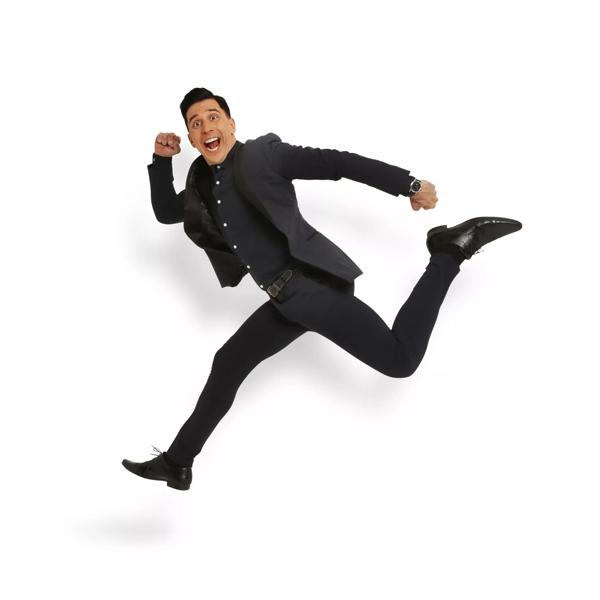 Russell Kane wears a black suit against a white background.