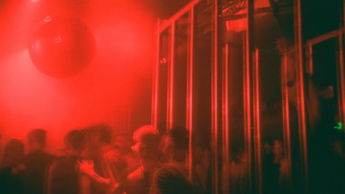 Hazy club scene of people dancing in moody red lighting.