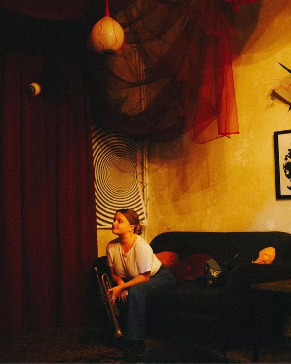An atmospheric room with prints hanging on the walls and a person holding a trumpet sitting on a sofa