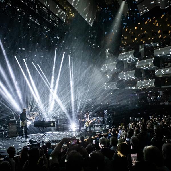 Guitarist Johnny Marr performs on stage at the Royal Festival Hall during Meltdown festival. The hall is dark and the stage is illuminated in a number of white spotlights. The audience are on their feet in the seats and in the boxes in the auditorium