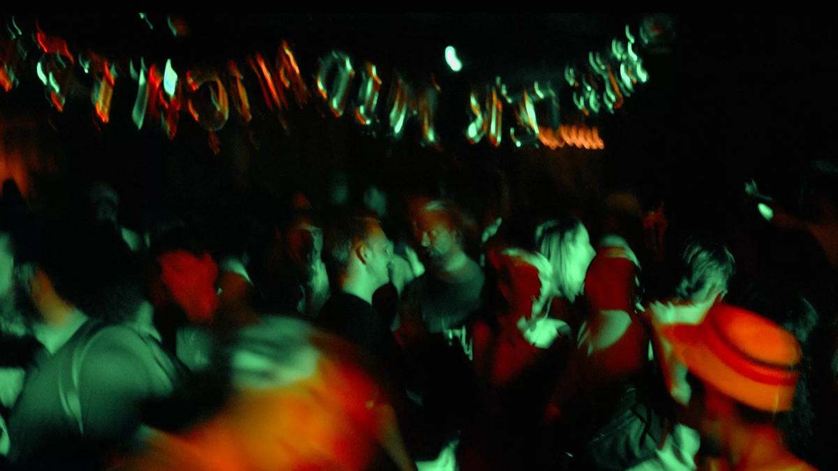 Crowd of people in a dark venue under green and red lighting with silver letter shape balloons hung above