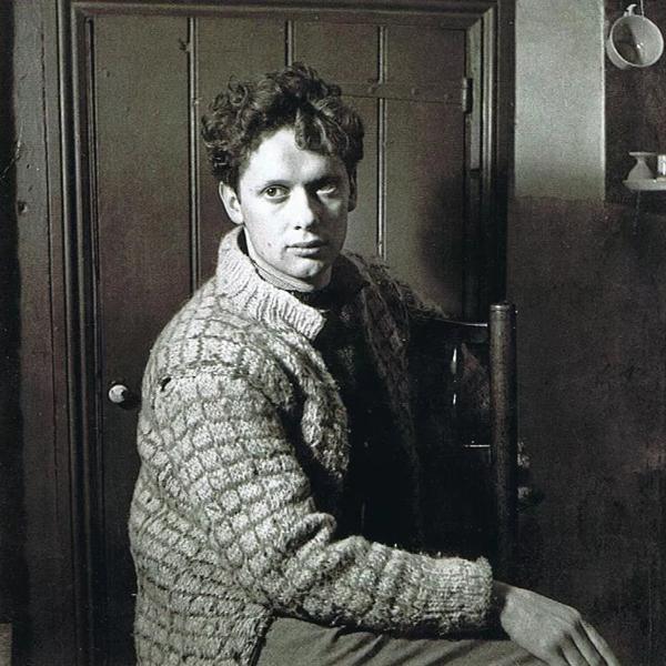 Dylan Tomas wearing a thick cardigan seated on a chair in a cottage