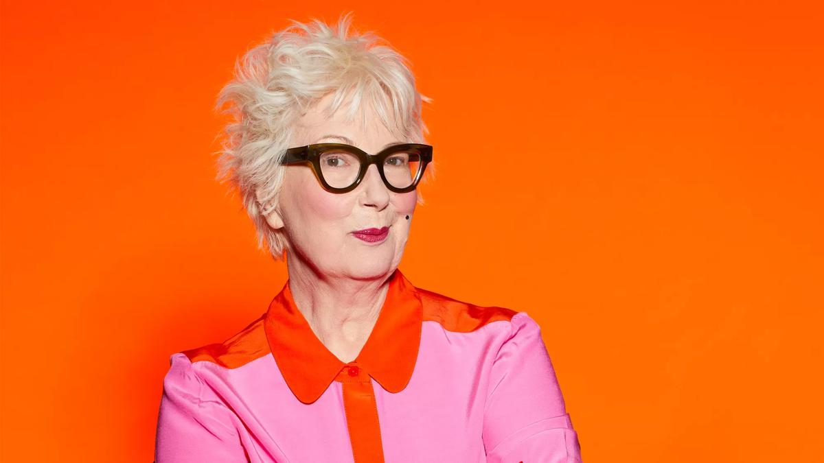 Jenny Eclair in a pink shirt  on an orange background 