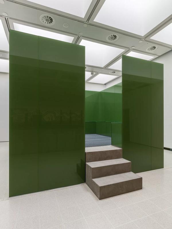 A cube made up of green walls with stairs leading up to seating 