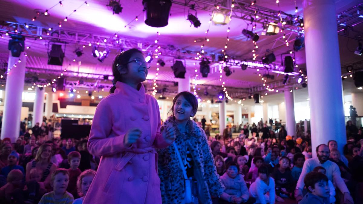 Two girls standing in front of a crowd in purple light