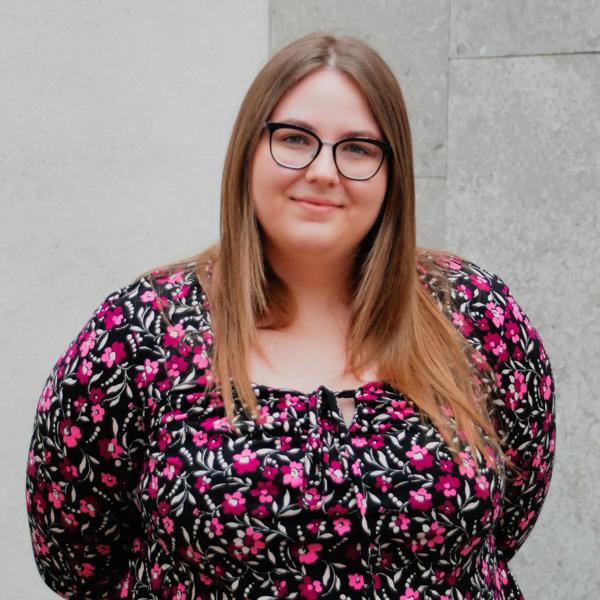 Deborah Strauss, a young White woman with glasses and long brown hair, wearing a floral print dress